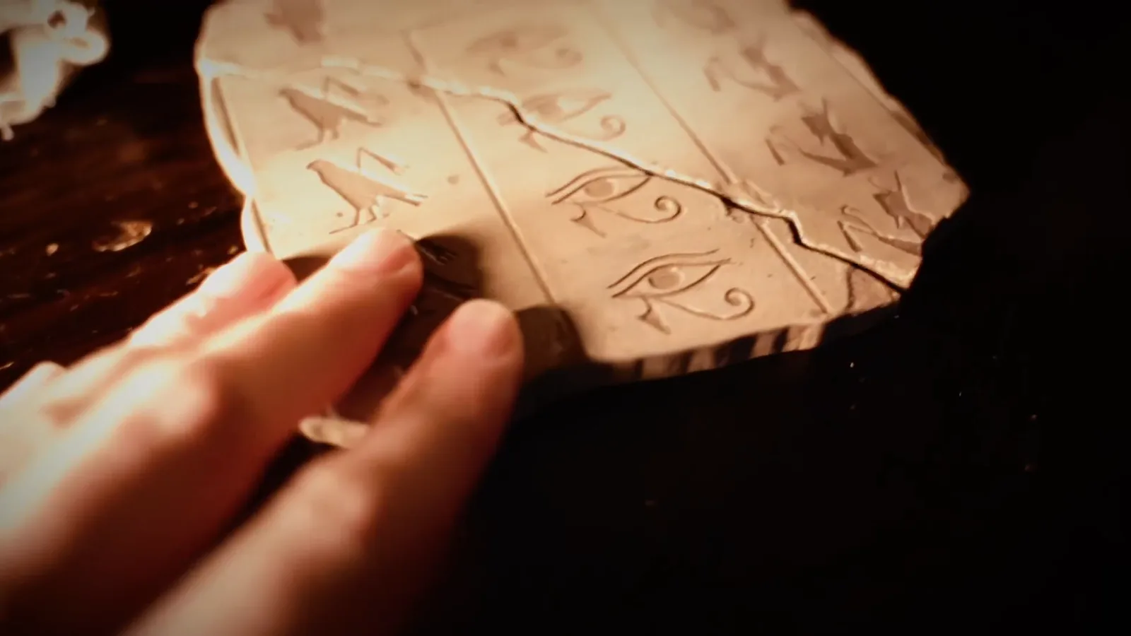 A hand holding a carved hieroglyph tablet with the Eye of Horus in Entombed
